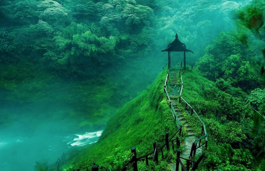 Vista de unas cascadas y un kiosko de madera en un parque lleno de naturaleza verde en Laos, uno de los paises para hacer turismo ecologico